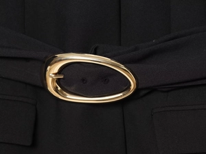 Gros plan d'une boucle ovale en métal doré sur la ceinture noire d'une veste blazer