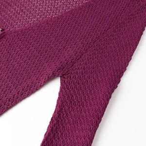 Detailed close-up of purple knit crochet fabric with openwork pattern and small metal button