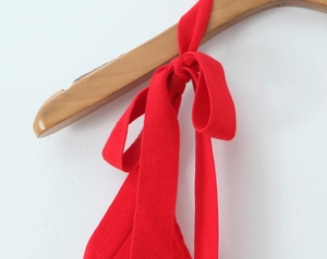 Detail of red knit dress showing shoulder straps tied into elegant bows on a wooden hanger