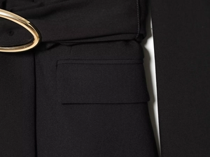 Détail d'un blazer noir avec une boucle de ceinture dorée et une poche à rabat