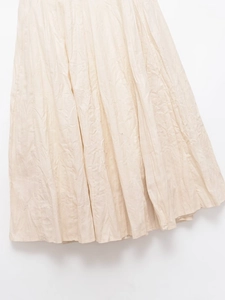 Close-up of cream pleated midi skirt showing fine vertical crinkle fabric texture