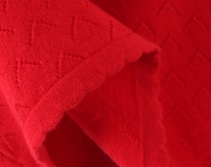 Macro view of red knit dress fabric showing intricate diamond texture and ribbed edge