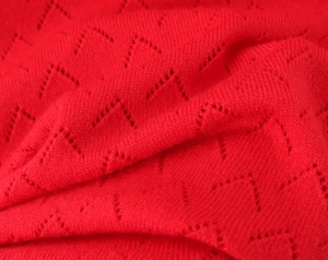 Macro shot of red knitted dress fabric with delicate chevron hollow pointelle texture