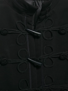 Détail des fermetures à brandebourgs et texture tissée sur cette veste chic noire