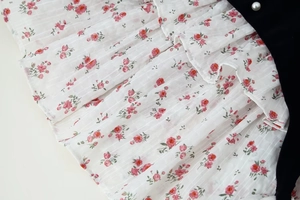 Detail of floral chiffon fabric with ruffled edges and black velvet pearl button accent