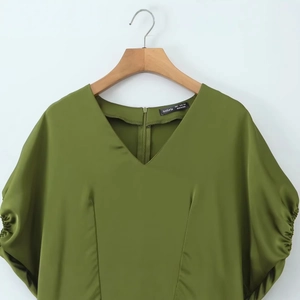 Grass green V-neck satin top with ruched short sleeves and asymmetrical hem on a hanger