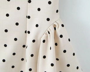 Detail of black polka dot pattern on cream fabric with side seam and ruffled hem edges