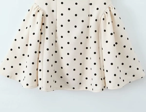 Detailed view of white pleated skirt fabric featuring black polka dots and gathered hem