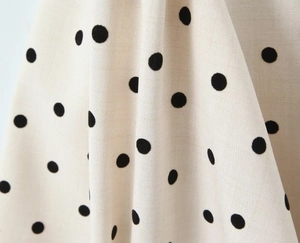 Close-up of light beige fabric with black polka dots showing smooth textile texture