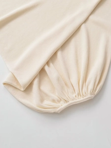 Detail shot of cream white knit top featuring fine texture and ruched cuff design