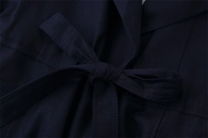 Dettaglio del trench blu navy in tessuto strutturato con un elegante nodo alla cintura