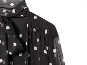 Detail of polka dot blouse showing bow tie neckline and sheer chiffon sleeve texture