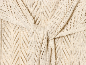 Detailed close-up of cream knit fabric with hollow wave patterns and twist knot detail