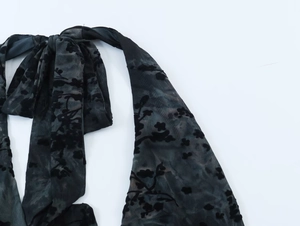 Détail du tissu en maille noire transparente avec flocage floral et nœud décoratif au cou