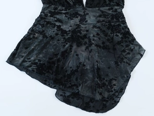 Détail du tissu en maille noire avec fleurs floquées et plis délicats sur l'ourlet