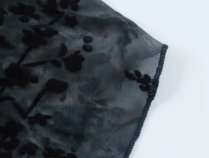 Vue détaillée du tissu en tulle noir avec flocage floral texturé et finition de couture soignée