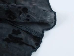 Vue macro d'un tissu en maille transparente avec motifs floqués noirs et coutures surjet