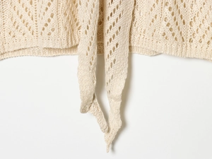 Detailed macro view of beige crochet knit fabric featuring diamond hollow pattern with ties
