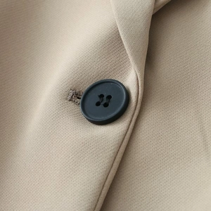 Detail view of a matte black four-hole button on a beige slim-fit blazer for women