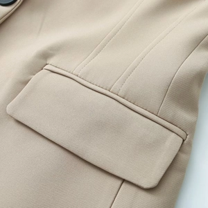 Detailed close-up of beige blazer pocket with black button and precise stitching finish