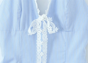 Detail of V-neckline with delicate white floral lace and bow on blue striped dress