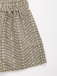 Détail du tissu vert olive avec broderie florale blanche et design ajouré à œillets