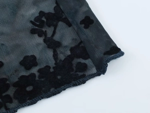 Gros plan sur tissu en maille noire avec flocage floral en velours et ourlet détaillé