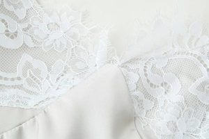 Dettaglio del pizzo floreale bianco e del tessuto di raso liscio su un abito sottoveste