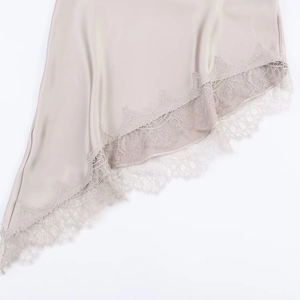 Close-up of champagne satin dress hem with intricate lace trim and asymmetrical cut