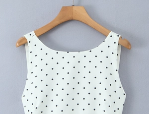 Detail of white sleeveless top with black polka dots hanging on a wooden hanger