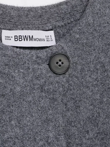 Détail d'un cardigan gris montrant la texture, un bouton noir et l'étiquette de taille