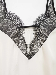 Detailansicht eines weißen Satin-Tops mit schwarzer Wimpernspitze und feinem V-Ausschnitt