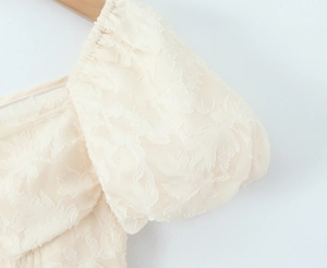 Détail du col carré et texture fleurie jacquard sur une robe crème à manches bouffantes