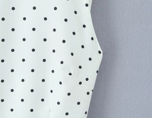 Close-up detail of smooth white fabric featuring a classic black polka dot pattern