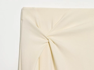 Detailed view of the elegant knot design and pleated texture on a cream midi skirt