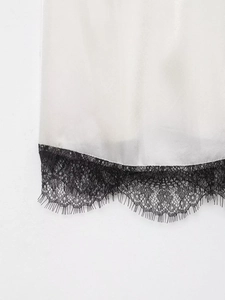 Detail eines weißen Satin-Tops mit exquisiter schwarzer Wimpernspitze und Seidentextur