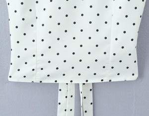 Detailed view of white polka dot fabric featuring hemline stitching and hanging tie straps