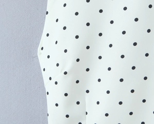 Close-up of high-quality white woven fabric with black polka dots and fine stitching