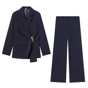 Détail d'un tailleur pantalon bleu marine avec veste cache-cœur et boucle sur fond blanc
