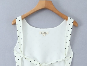 Detail of white polka dot chiffon top featuring back lace-up straps and brand neck label