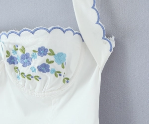Detail of white dress with blue floral embroidery and scalloped neckline edge