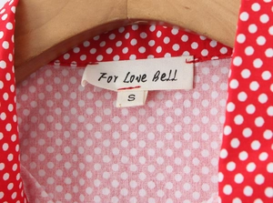 Detailed close-up of brand label and red polka dot fabric on the slim-fit short sleeve set