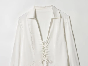 Detail of white satin shirt featuring a deep V-neckline and elegant lace-up front design