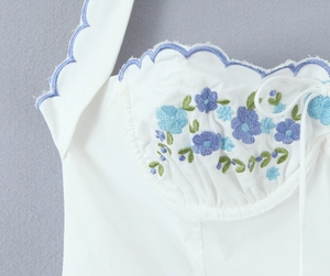 Detail of white dress featuring blue floral embroidery and scalloped neckline edges