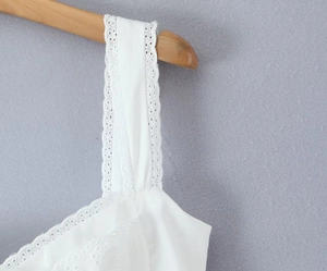 Close-up of white summer dress featuring intricate lace trim and floral embroidery detail
