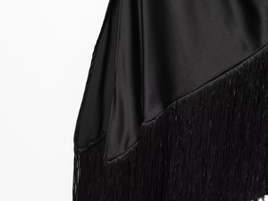 Detailed close-up of glossy black satin fabric and fringe trim on a chic summer dress