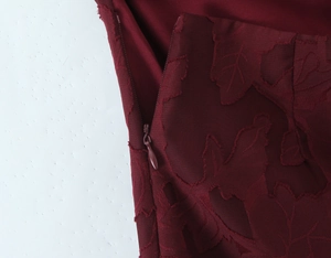 Detailed macro view of burgundy dress featuring floral jacquard fabric and invisible zipper