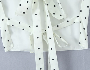 Close-up of a stylish black polka dot bow tie detail on a summer white fabric top