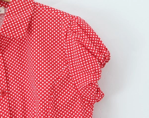 Detail of red shirt with white polka dots featuring puff sleeves and a resin button