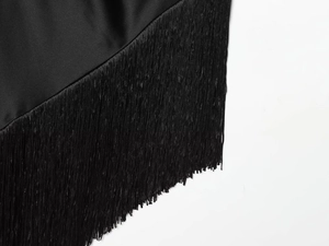 Detail of elegant black satin fabric with delicate fringe tassels on the dress hemline